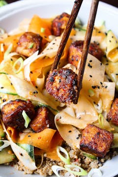 crispy tofu being placed on top of a bibimbap salad 