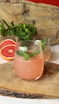 A mocktail on a chopping board with a chopped grapefruit.