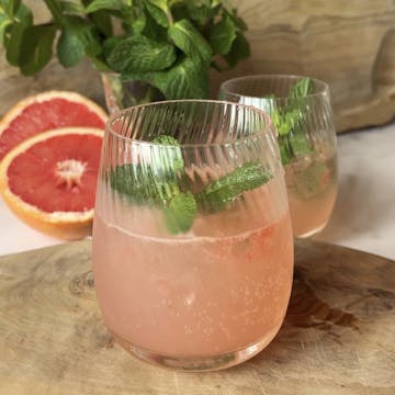 A mocktail on a chopping board with a chopped grapefruit.