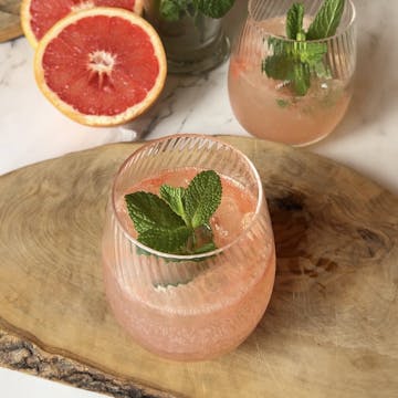 A mocktail on a chopping board with a chopped grapefruit.