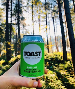 A can of Toast pale ale, held with a forest in the background. 