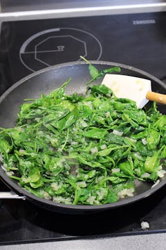 Spinach being fried in a pan with onion. 
