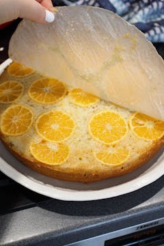 The baking paper at the bottom of the tray being peeled off, revealing the clementines beneath. 