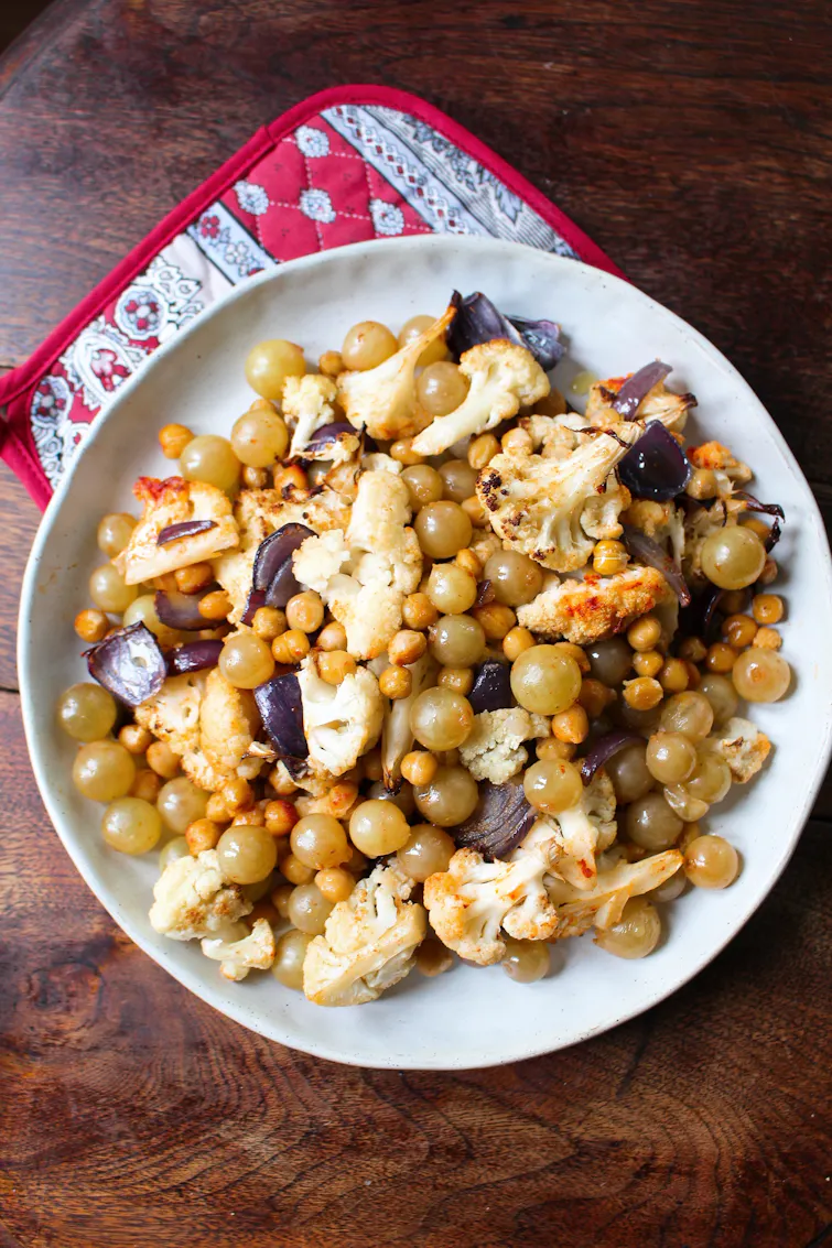 Roasted chickpeas, cauliflower, grapes piled onto a white plate. 