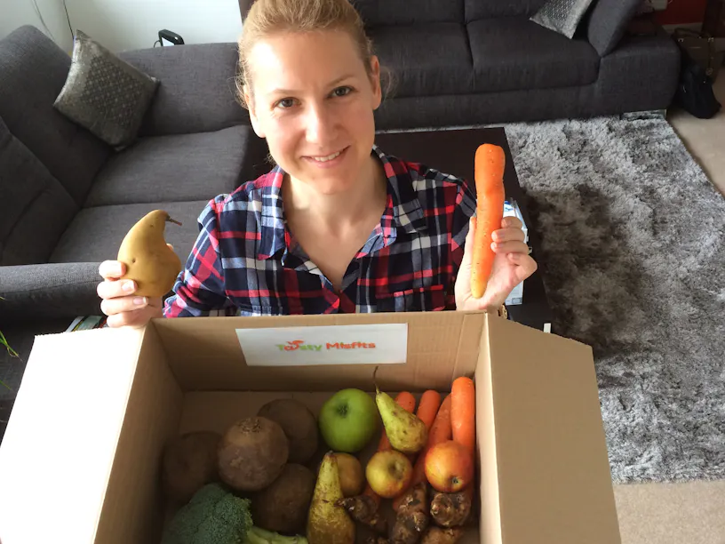 Emilie Vanpoperinghe holding a box filled with fruit and veg with the name Tasty Misfits