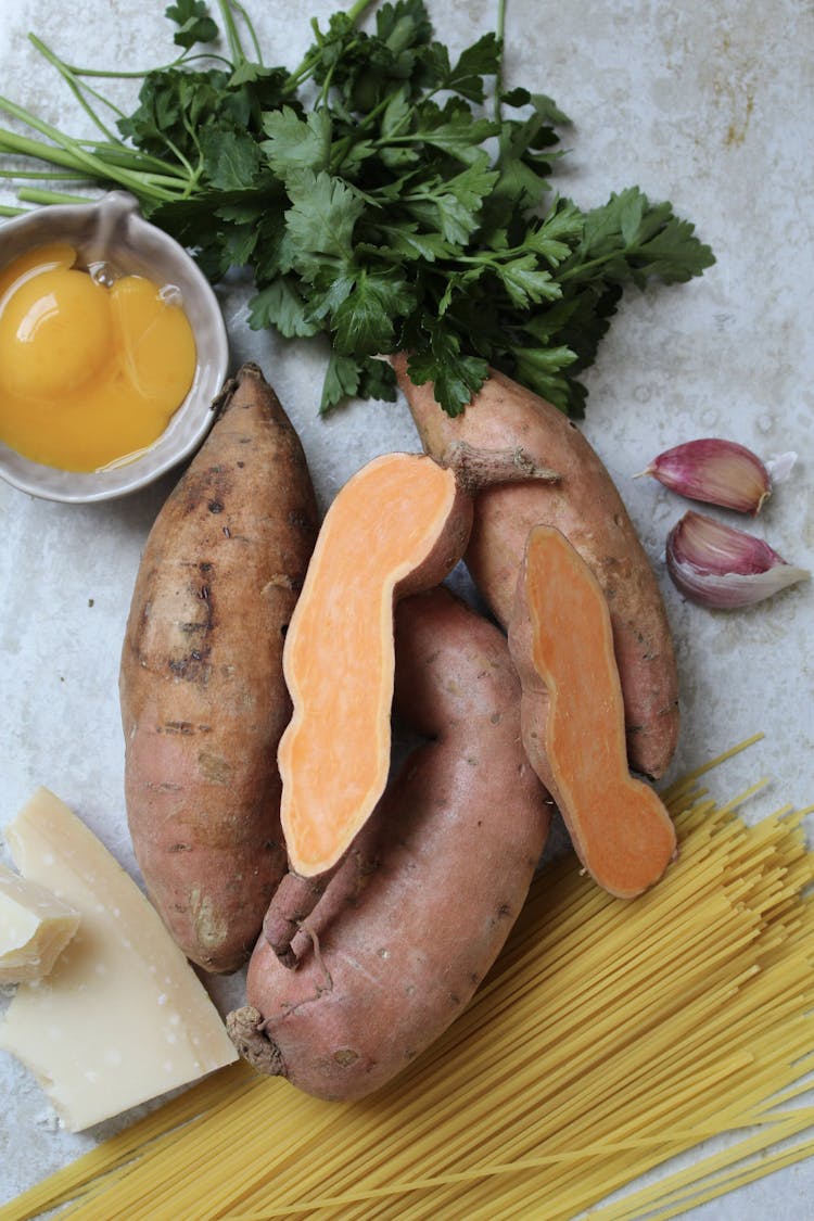 A pile of sweet potatoes with dried spaghetti, egg yolks, coriander, and 2 cloves of garlic.
