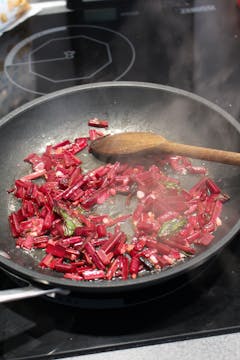 beetroot stalks being fried on a frying pan