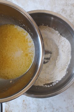 Water, olive oil, honey, and yeast being poured into a well of flour and salt. 