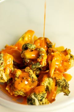 Buffalo sauce being poured over battered broccoli.