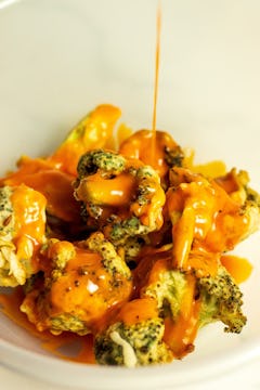 Buffalo sauce being poured over battered broccoli. 