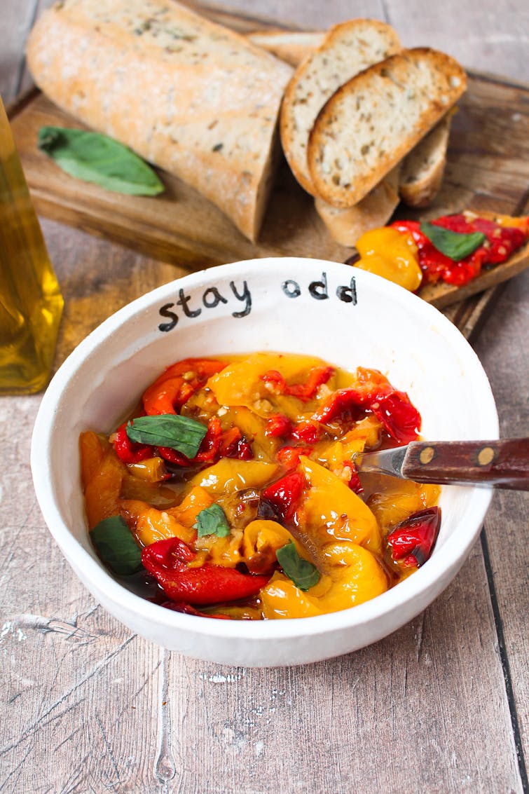 A bowl of marinated roasted peppers. There's a chopped baguette in the background. 