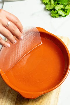 Rice paper being soaked in warm water in a bowl.
