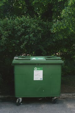 recycling bin in front of green bushes 