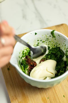 in a bowl, blended coriander, chilli flakes and mayonnaise being mixed 