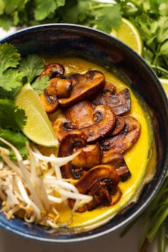 mushroom laksa bowl with golden broth, top with mushrooms, beansprouts, slice of lime and coriander