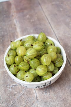 white bowl of fresh gooseberries on a wooden table