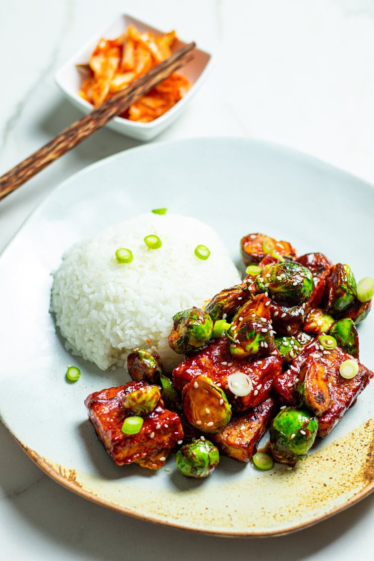 white rice, sprouts and tofu sprinkled with sesame seeds and sliced spring onion on a plate. Small side of kimchi