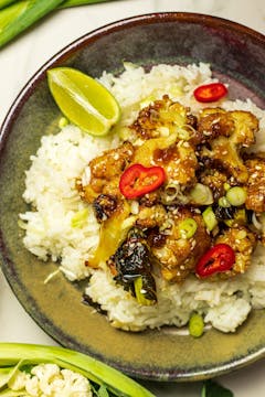 sticky honey sesame cauliflower served with rice in a bowl garnished with red chilli slices, spring onions and slice of lemon