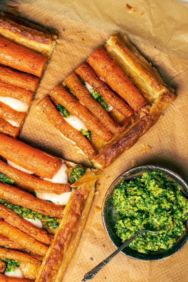 A slice of Caramelised Carrot Tart with a bowl of carrot top pesto