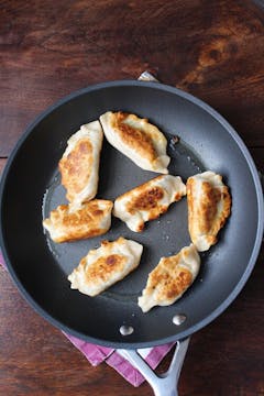 7 Potstickers being fried in a pan. 