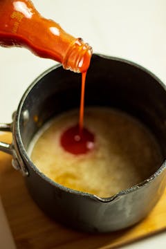 Buffalo sauce being added to a pan of melted butter. 