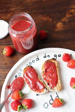 2 slices of bread with strawberry jam on a plate garnished with whole strawberry all over