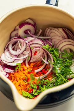 in a large bowl, grated carrots, carrot tops, sliced onion and seasoning