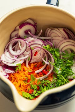 in a large bowl, grated carrots, carrot tops, sliced onion and seasoning 