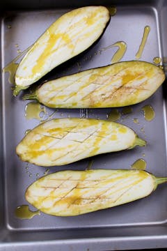 halved aubergines drizzled in oil on a baking tray 