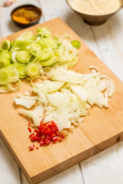 Sliced leeks, onions, garlic, ginger, and chilli on a chopping board. 