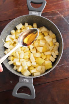 chopped apples in a sauce pan with maple syrup being added with a spoon