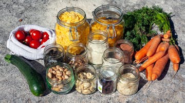 Jars of different nuts and dried fruits, carrots, one courgette and cherry tomatoes on the side