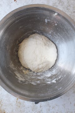 The ingredients for the pizza dough have been mixed to form a smooth dough. The dough is formed into a large ball in the center of the bowl. 