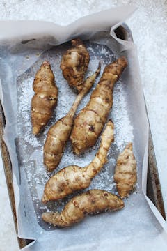 7 whole Jerusalem Artichokes on seasoned with sea salt on a baking tray with baking sheet