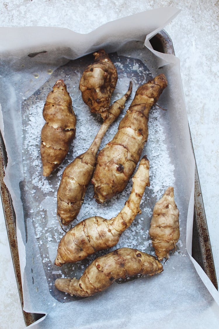 7 whole Jerusalem Artichokes on seasoned with sea salt on a baking tray with baking sheet
