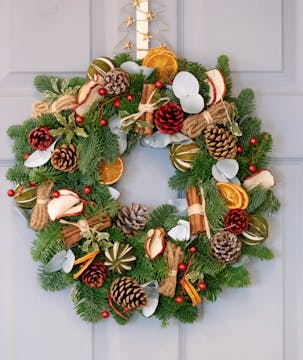 A foraged Christmas wreath with cinnamon sticks, pinecones, dried orange and apple slices, and cranberries. 