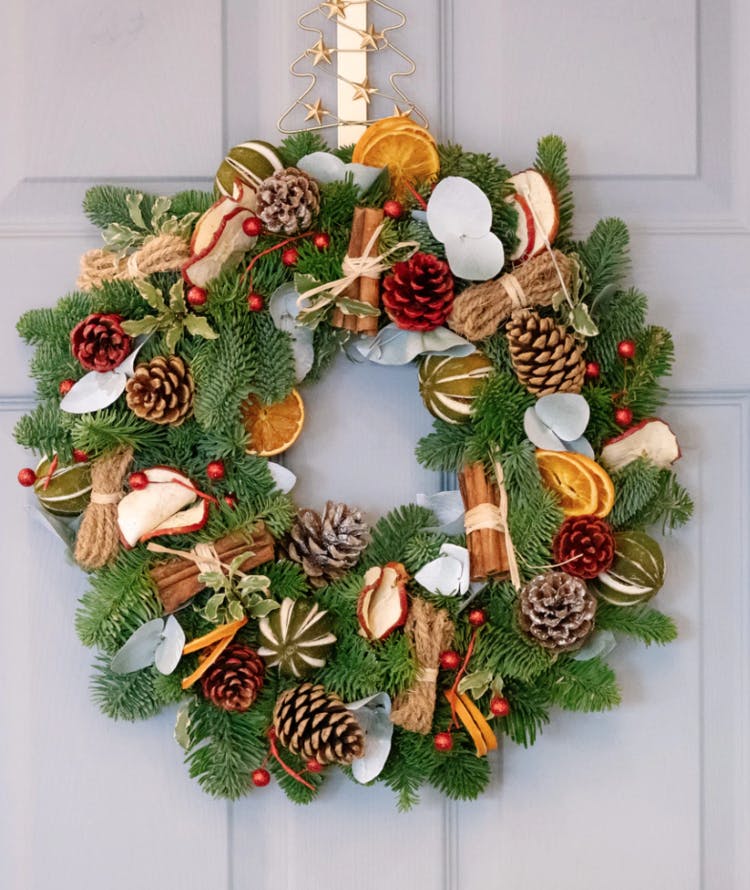 A foraged Christmas wreath with cinnamon sticks, pinecones, dried orange and apple slices, and cranberries. 