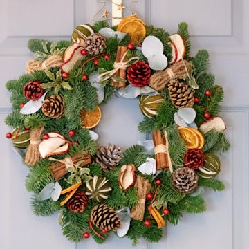 A foraged Christmas wreath with cinnamon sticks, pinecones, dried orange and apple slices, and cranberries. 