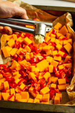 Garlic being crushed into a tray with squash and peppers.