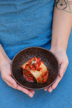 2 hands holding a bowl of kimchi