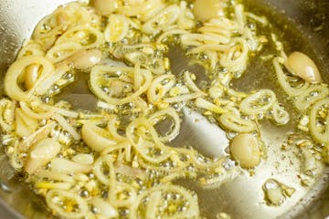 Onions being cooked in olive oil in a pan with garlic. 