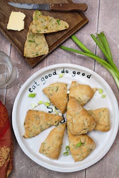 plate of 7 spring onion scones garnished with spring onion and on the side 2 slice of toasted spring onion scones, slice of butter and butterknife.