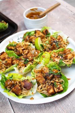 Peanut butter tofu lettuce wraps on a white plate with a bowl of sauce. 