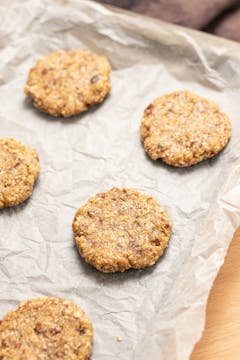 Date, tahini and oat cookies spread out on a lined baking tray.