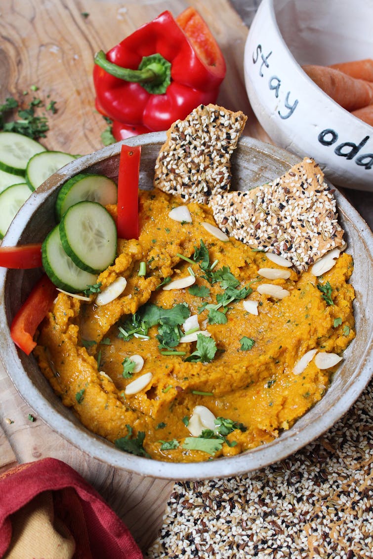 Harissa roasted carrot dip served in a bowl with red bell peppers, cucumber and bread