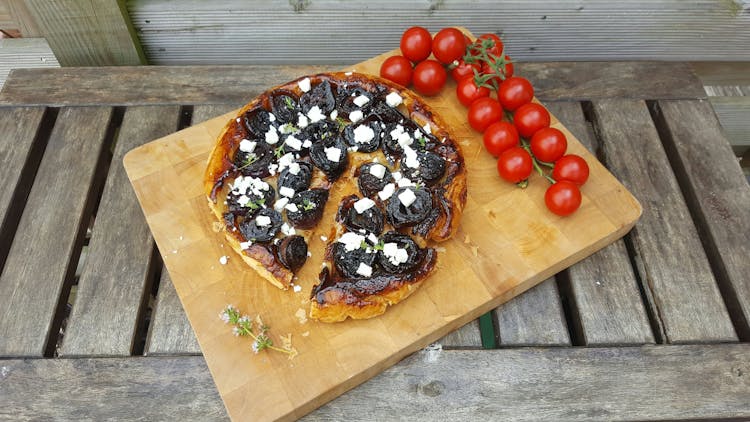 A caramelised red onion tart tatin on a chopping board, with a bunch of vine tomatoes next to it.