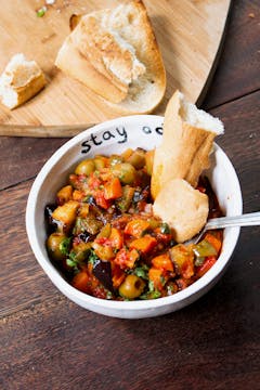 carrot caponata in a white bowl with crusty bread dipped in