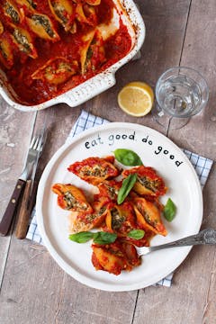 A plate of baked spinach pasta shells next to the oven tray with the rest in it. 