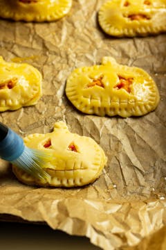 An assembled empanada being brushed with an egg glaze, sealed with a fork.