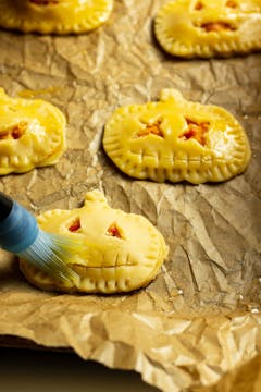 An assembled empanada being brushed with an egg glaze, sealed with a fork. 